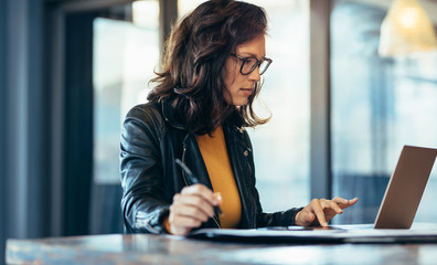 Businesswoman making notes looking at a laptop