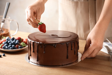 Baker decorating fresh delicious homemade chocolate cake with berries on table, closeup