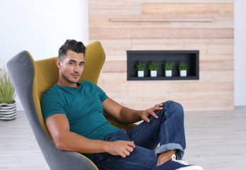 Wall Mural - Portrait of handsome young man sitting in armchair at home