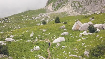 Wall Mural - drone view woman walking on mountain trail among big stones on green grass