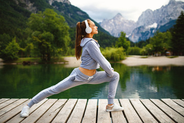 Sticker - Young sports woman stretching legs at dock on the lake in the mountains