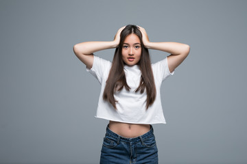 Frustrated confused asian woman keeping hands in her hair and shocked over gray background