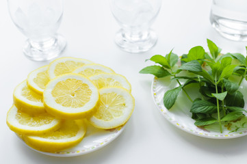 Lemon slices, fresh mint on a plates and two glasses with ice cubes. Ingredients for homemade lemonade, perfect for summer.