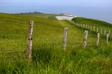 Post And Wire Fence Leading Along A Field To A Chalk Cliff In The Distance