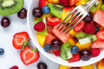 Wall Mural - Bowl of healthy fresh fruit salad with fork on white marble background. healthy food. close up