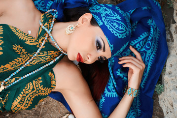 Beautiful woman lying down on cliff. A lovely caucasian girl lies in a blue scarf dress and dreamed. Top view.