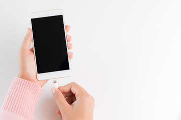 Woman hands connecting charger to smartphone on white table background.