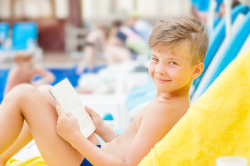 Wall Mural - Little boy reading a book by the pool.  Relaxation resting vacations concept