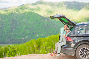 Young couple sitting in hatchback car with mountain background. Space for text