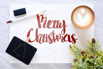 Poster - Top view of red merry christmas text on marble table with blackboard, pencil, eraser pine leaf and coffee cup.holiday greeting card