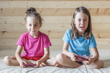 Two little girls play in video game with joystick in their hands