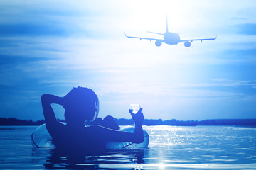 Wall Mural - A woman floating on an inflatable circle and looking at a flying plane at night