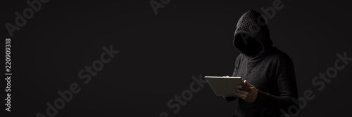 Cuadros en Lienzo Faceless man in a hoodie with a hood holds a tablet in his hands