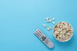 © Alex - Bowl with popcorn and remote control for TV on a blue background