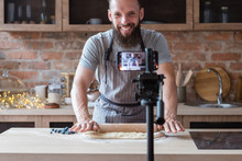 Food Blogger Streaming Live. Bearded Hipster Man Communicating With Subscribers Through Phone Camera. Chef Rolling Out Dough With A Pin.