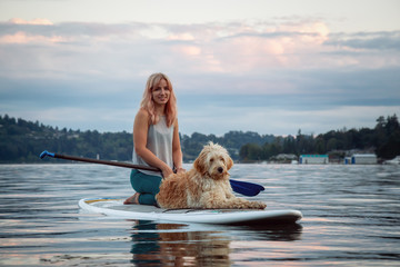 Girl with a dog on a paddle board during a vibrant summer sunset. Taken in Deep Cove, North Vancouver, BC, Canada.