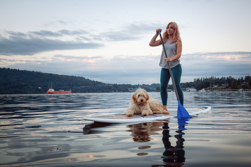 Girl with a dog on a paddle board during a vibrant summer sunset. Taken in Deep Cove, North Vancouver, BC, Canada.