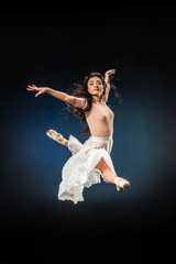 Wall Mural - young ballerina in elegant clothing jumping on dark backdrop