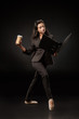 © LIGHTFIELD STUDIOS - attractive businesswoman in suit and ballet shoes with folder and coffee to go posing on black backdrop