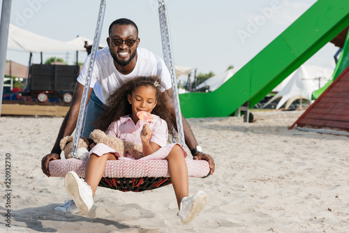 Smiling African American Father Pushing Daughter On Spider
