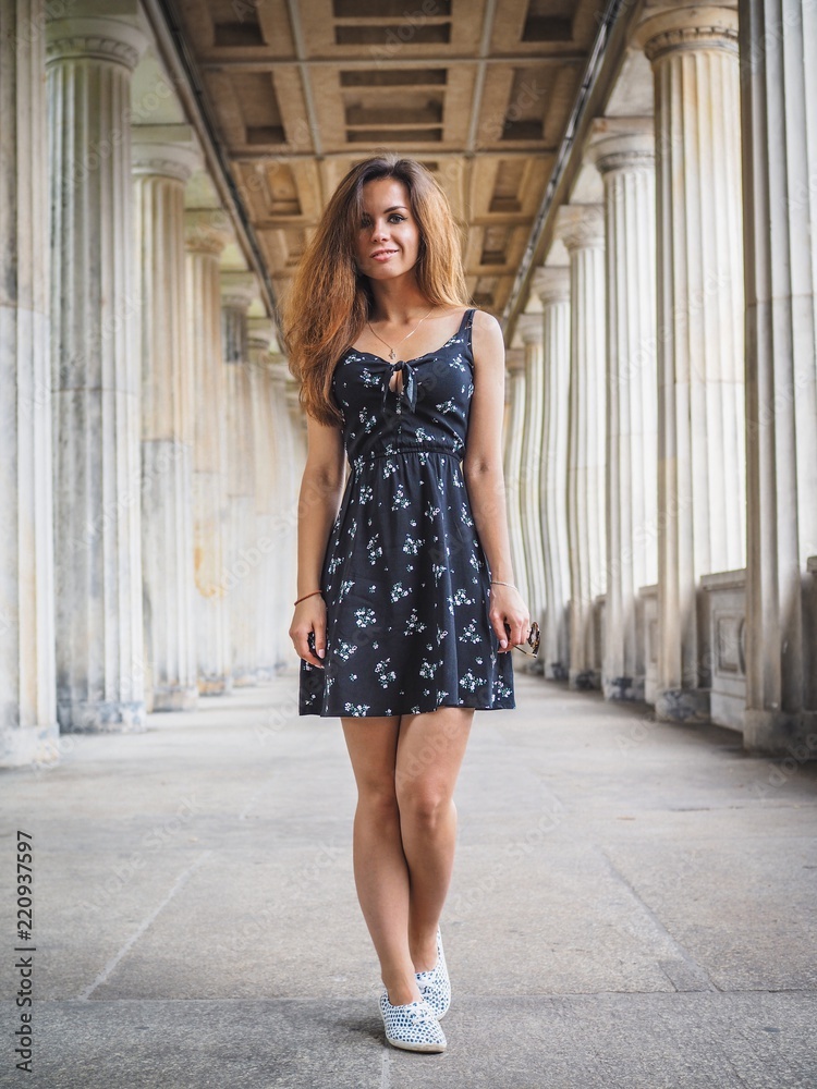 brunette short dress Brunette girl with long hair in black short dress stands between a long row  of columns Stock Photo