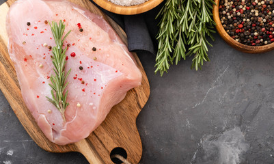 Raw turkey fillets on black cutting board with spices and herbs. Cooking ingredients. Natural healthy food concept. Top view with space for text