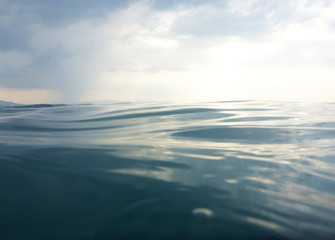 Background texture of clear, blue sea at water level and a cloudy evening sky