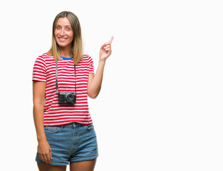 Poster - Young beautiful woman taking pictures using vintage photo camera over isolated background with a big smile on face, pointing with hand and finger to the side looking at the camera.