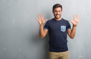 Handsome young man over grey grunge wall showing and pointing up with fingers number ten while smiling confident and happy.