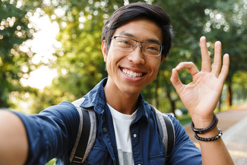 Sticker - Smiling asian male student in eyeglasses making selfie