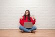 © Krakenimages.com - Young brunette woman sitting on the floor over white brick wall paying holding dollars with surprise face pointing finger to himself
