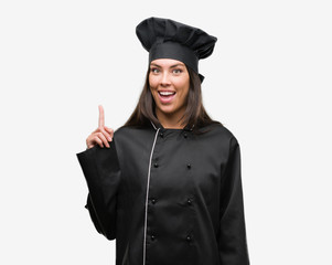 Sticker - Young hispanic cook woman wearing chef uniform surprised with an idea or question pointing finger with happy face, number one