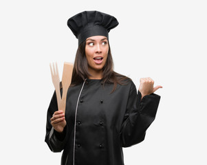 Sticker - Young hispanic cook woman wearing chef uniform pointing and showing with thumb up to the side with happy face smiling