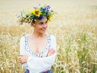 Ukrainian girl in a beautiful wreath walks through the summer meadow. The girl is dressed in ethnic clothes with embroidery. Feast of Ivan Kupala