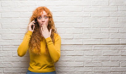 Poster - Young redhead woman standing over brick wall talking on the phone cover mouth with hand shocked with shame for mistake, expression of fear, scared in silence, secret concept