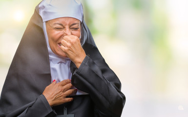 Poster - Middle age senior christian catholic nun woman over isolated background smelling something stinky and disgusting, intolerable smell, holding breath with fingers on nose. Bad smells concept.