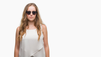 Sticker - Young blonde woman wearing sunglasses with serious expression on face. Simple and natural looking at the camera.