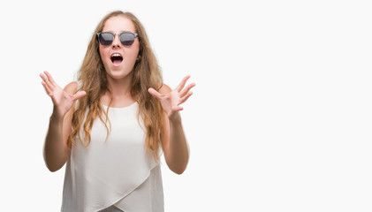 Poster - Young blonde woman wearing sunglasses crazy and mad shouting and yelling with aggressive expression and arms raised. Frustration concept.