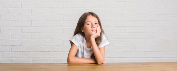 Young hispanic kid sitting on the table at home thinking looking tired and bored with depression problems with crossed arms.