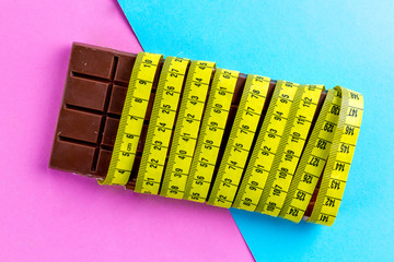 Diet concept. Losing weight concept. Chocolate and yellow measuring tape on a colored background