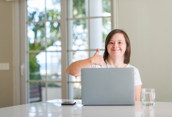 Down syndrome woman at home using computer laptop happy with big smile doing ok sign, thumb up with fingers, excellent sign