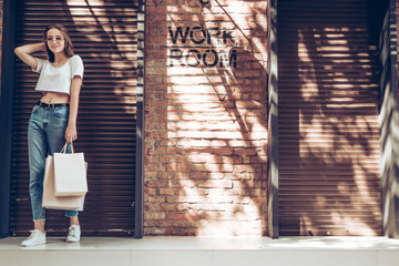 Young smiling girl with shopping bag wearing white t-shirt and blue jeans near brick wall.Lifestyle concept.