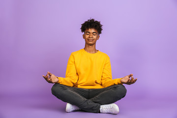 Poster - Portrait of relaxed african american boy sitting in lotus pose and meditating with closed eyes, isolated over violet background