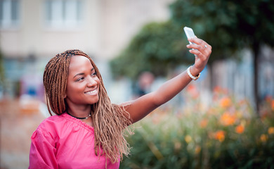 Wall Mural - Happy African girl using mobile phone and making selfie at city street