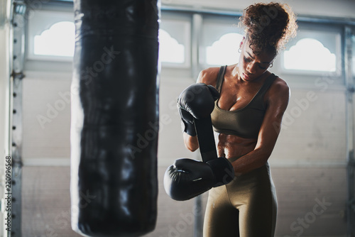 african american woman covered in sweat from boxing punching bag taking off gloves