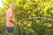 senior old man pouring harvest with water in summer garden outdoor