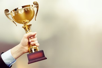 close-up human hand holding golden trophy on blurred blue