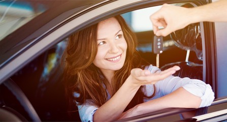 Young beautiful woman taking keys while sitting at car