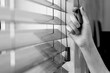 The woman's right hand holds one of the control strings of the wooden shutters on the window. black and white.