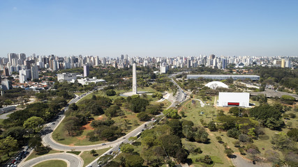 Wall Mural - Aerial view of Ibirapuera park in Sao Paulo city, obelisk monument. Prevervetion area with trees and green area of Ibirapuera park. Office buildings and apartments in the background on a sunny day.